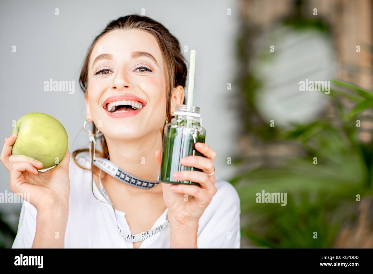 Portrait of a young woman with apple and smoothie drink indoors. Healthy eating and wight loss concept Stock Photo