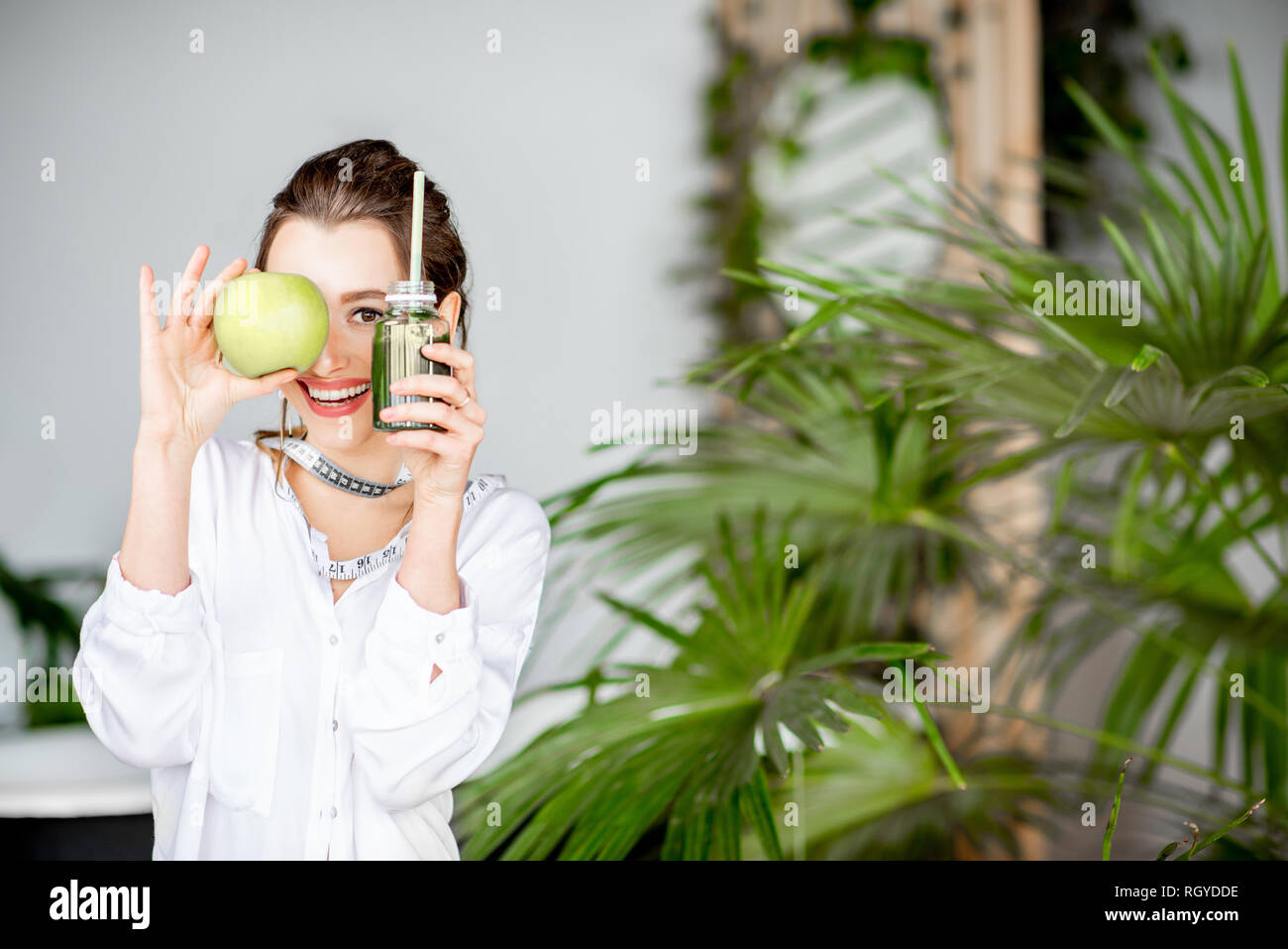 Portrait of a young woman with apple and smoothie drink indoors. Healthy eating and wight loss concept Stock Photo