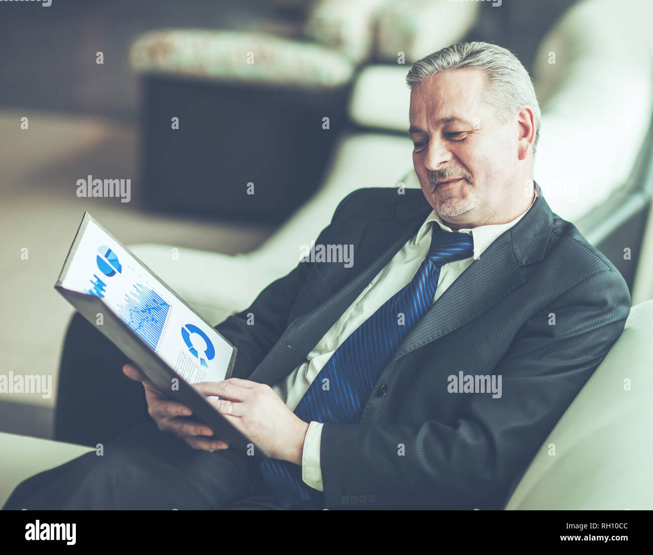 foreground is an experienced financier with financial charts sitting in the chair in front of the office. Stock Photo