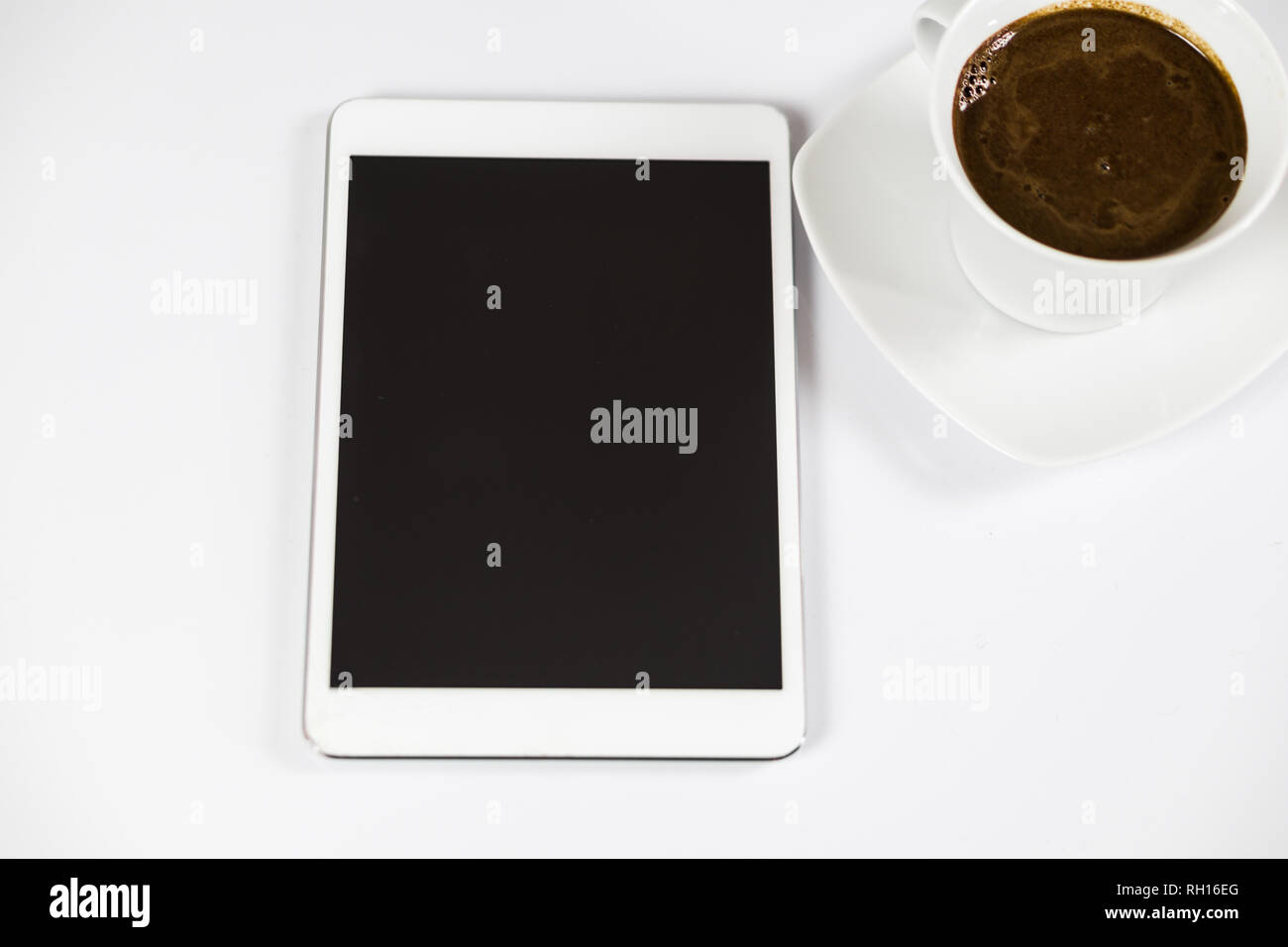 Computer tablet with black empty screen next to coffee. The tablet is on the white table. View from the top. Close-up. Stock Photo