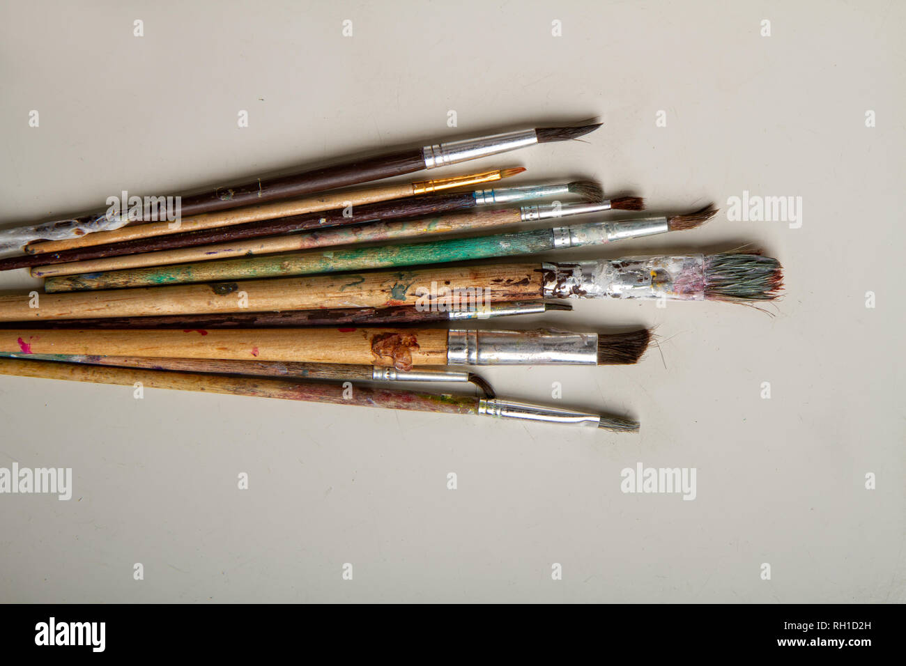 A collection of well used art paint brushes with a highly colourful  abstract artwork as a background Stock Photo - Alamy