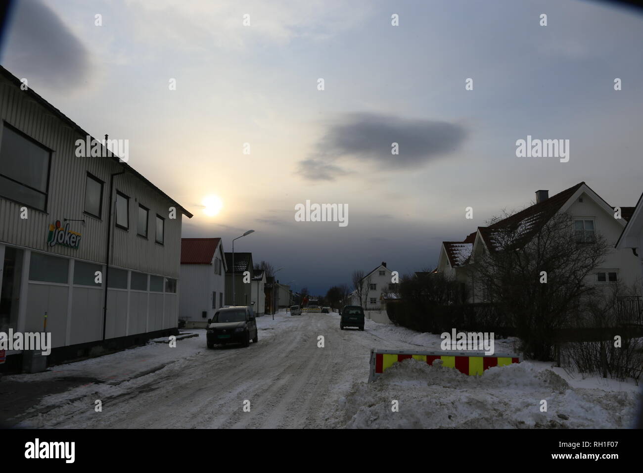 verschneite Straße in Bodö Norwegen. Im Hintergrund baut sich eine Schneefront auf. Gegenlicht, verschleierte Sonne Stock Photo