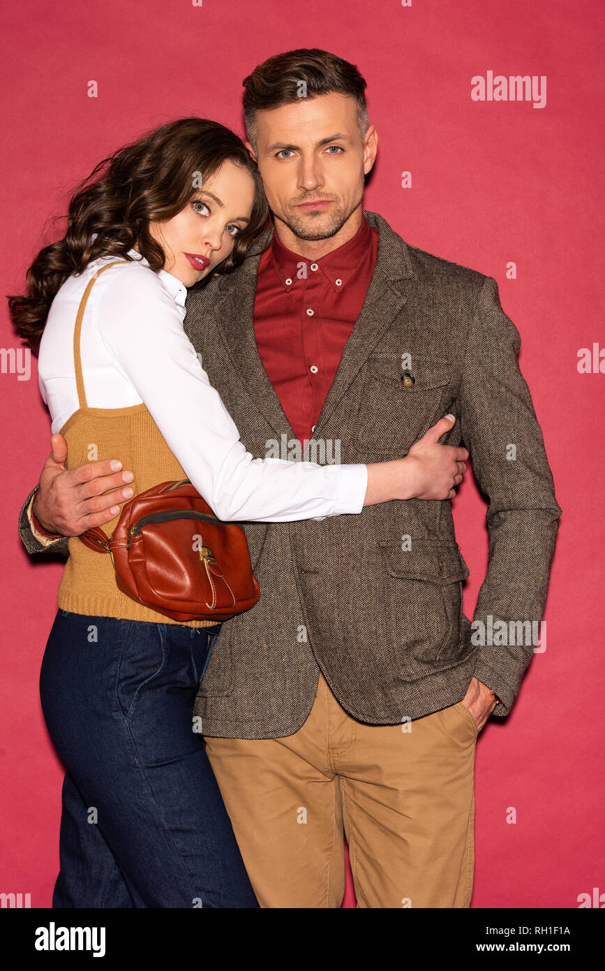 beautiful fashionable couple in formal wear embracing and posing on red background Stock Photo