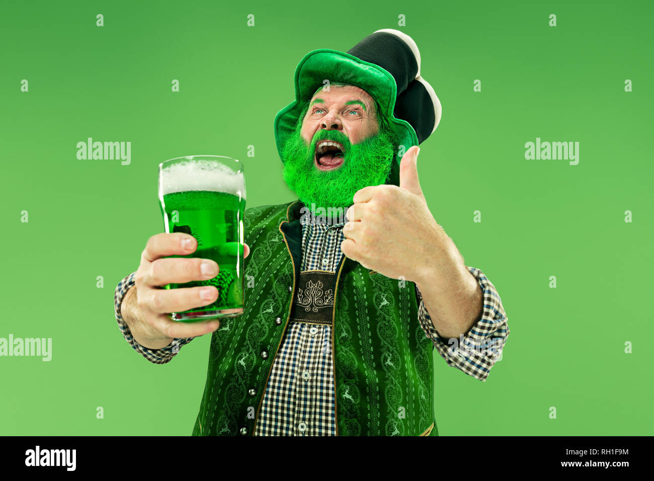 A smiling happy senior man in a leprechaun hat with green beer at studio. He celebrates St. Patrick's Day. The celebration, festive, beer, holiday, alcohol, party concept Stock Photo