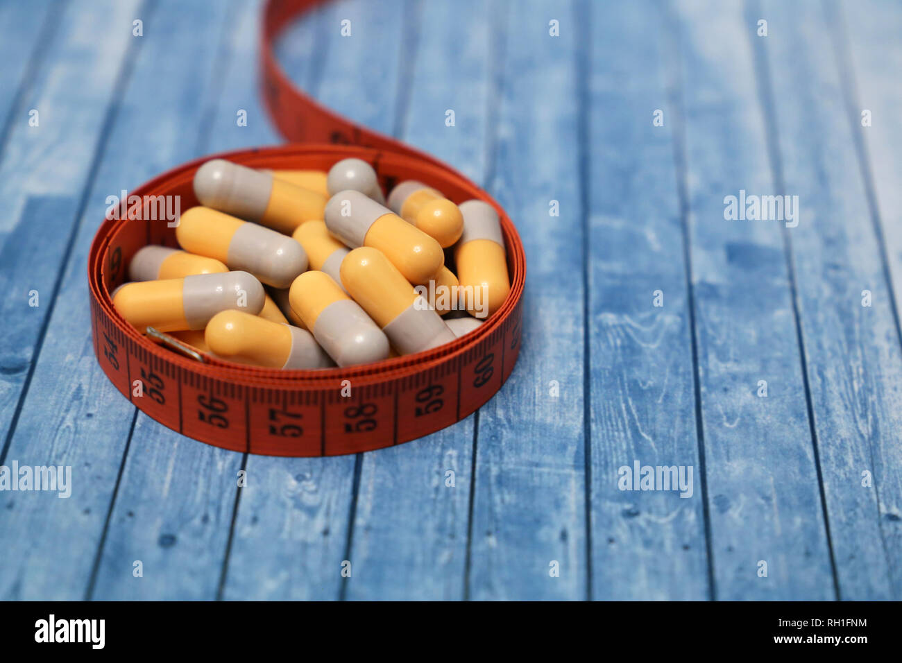 Diet pills, weight loss remedy. Medication in capsules and measuring tape on wooden table Stock Photo