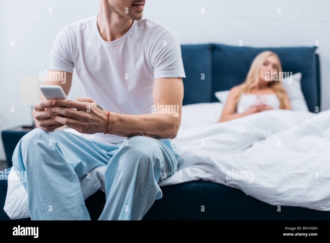 cropped shot of young man in pajamas using smartphone while jealous