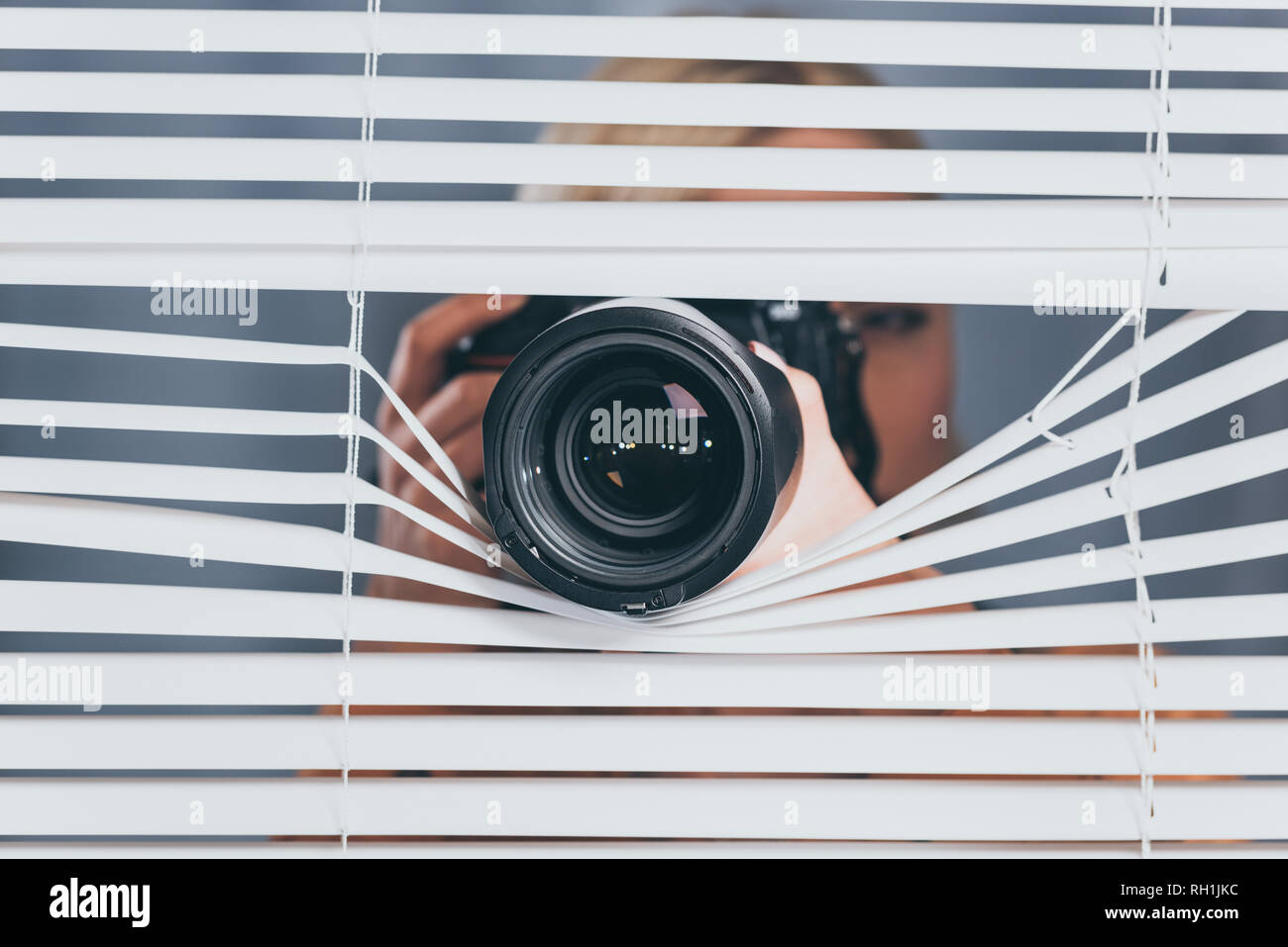 young woman photographing with camera and spying through blinds Stock Photo