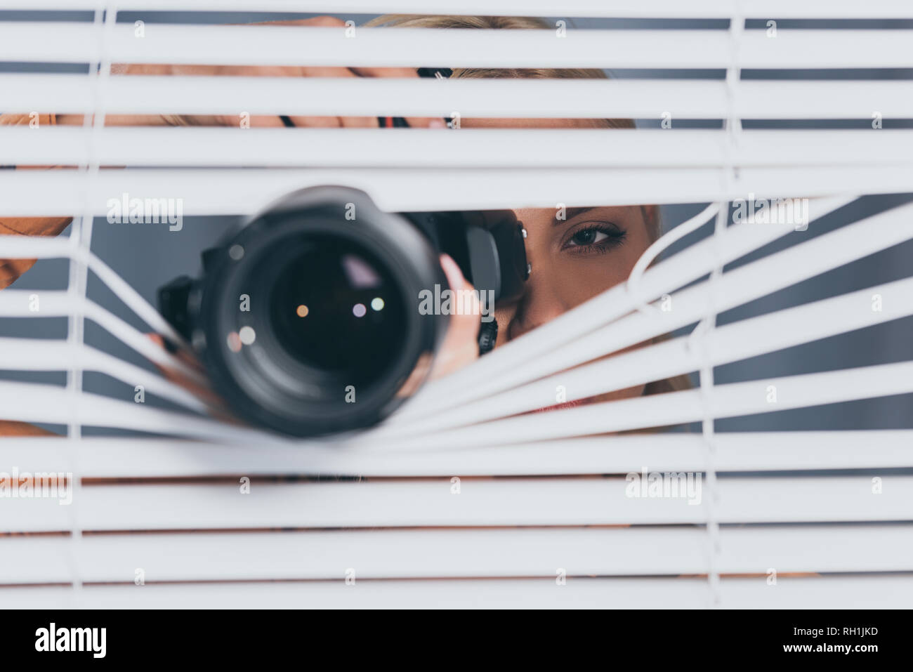 close-up view of camera and young woman taking pictures and spying through blinds Stock Photo