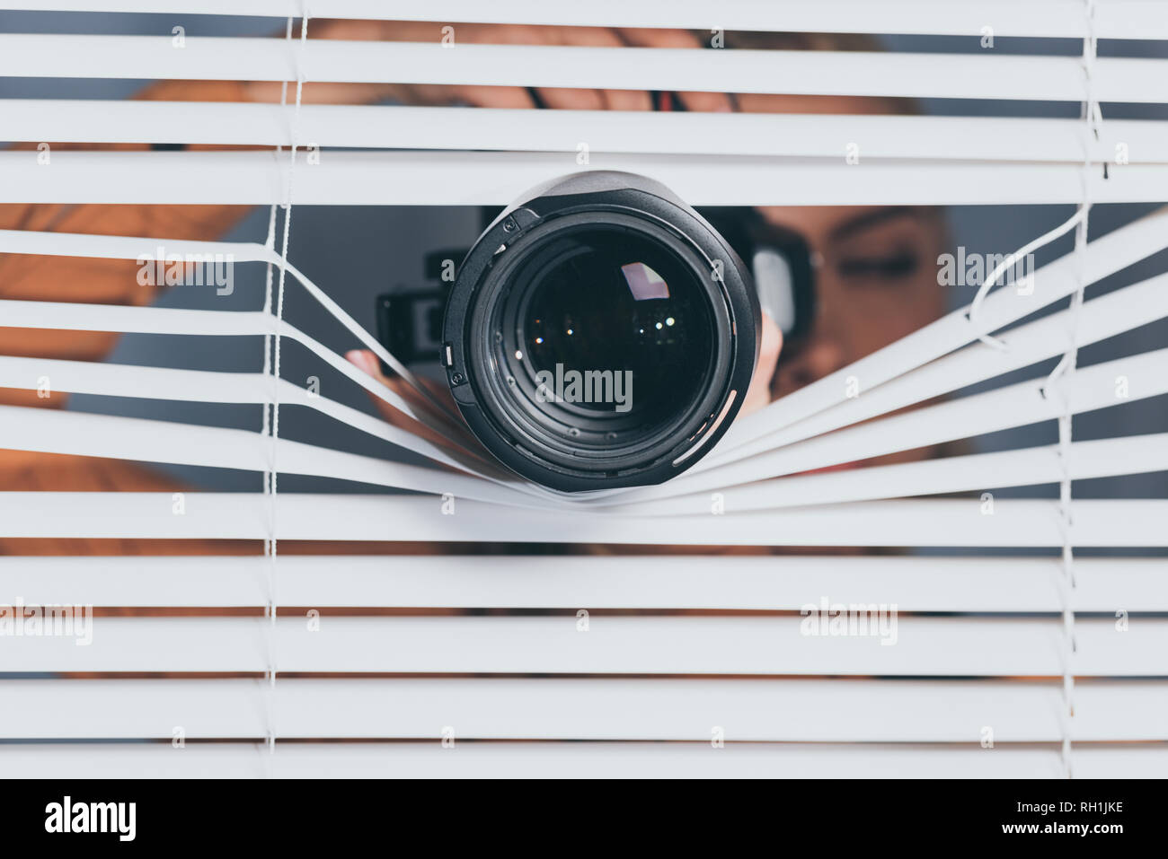 close-up view of camera and young woman spying through blinds Stock Photo