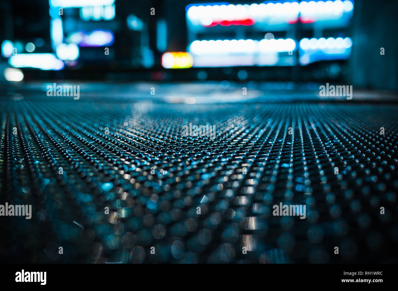 Abstract night city background with wet street sewer grate on urban road, close-up photo with selective focus Stock Photo