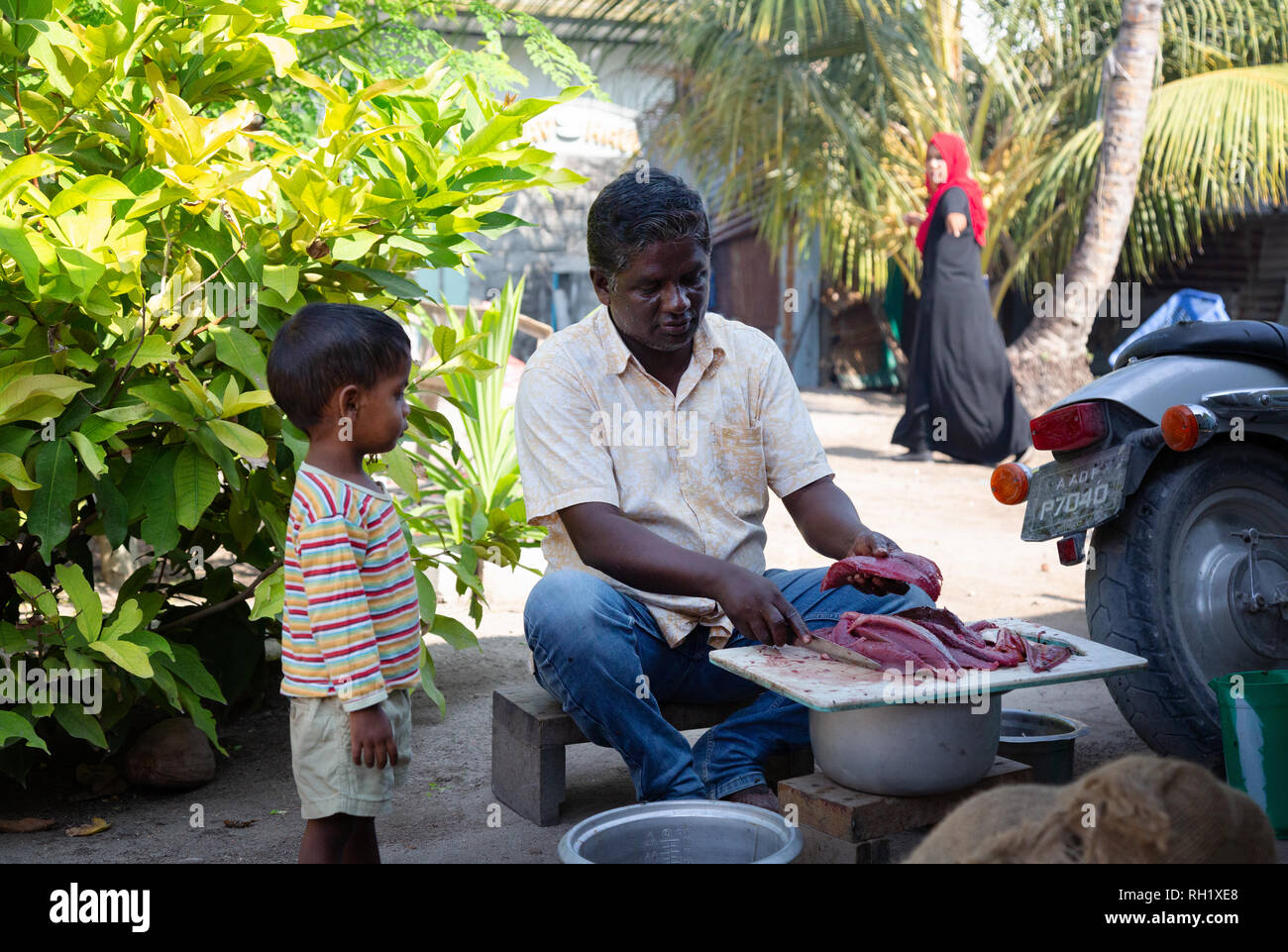 Muslim family - a father prepares fish for a meal watched by his young son and wife,  Ukulhas island, Alif Alif atoll, the Maldives, Asia Stock Photo