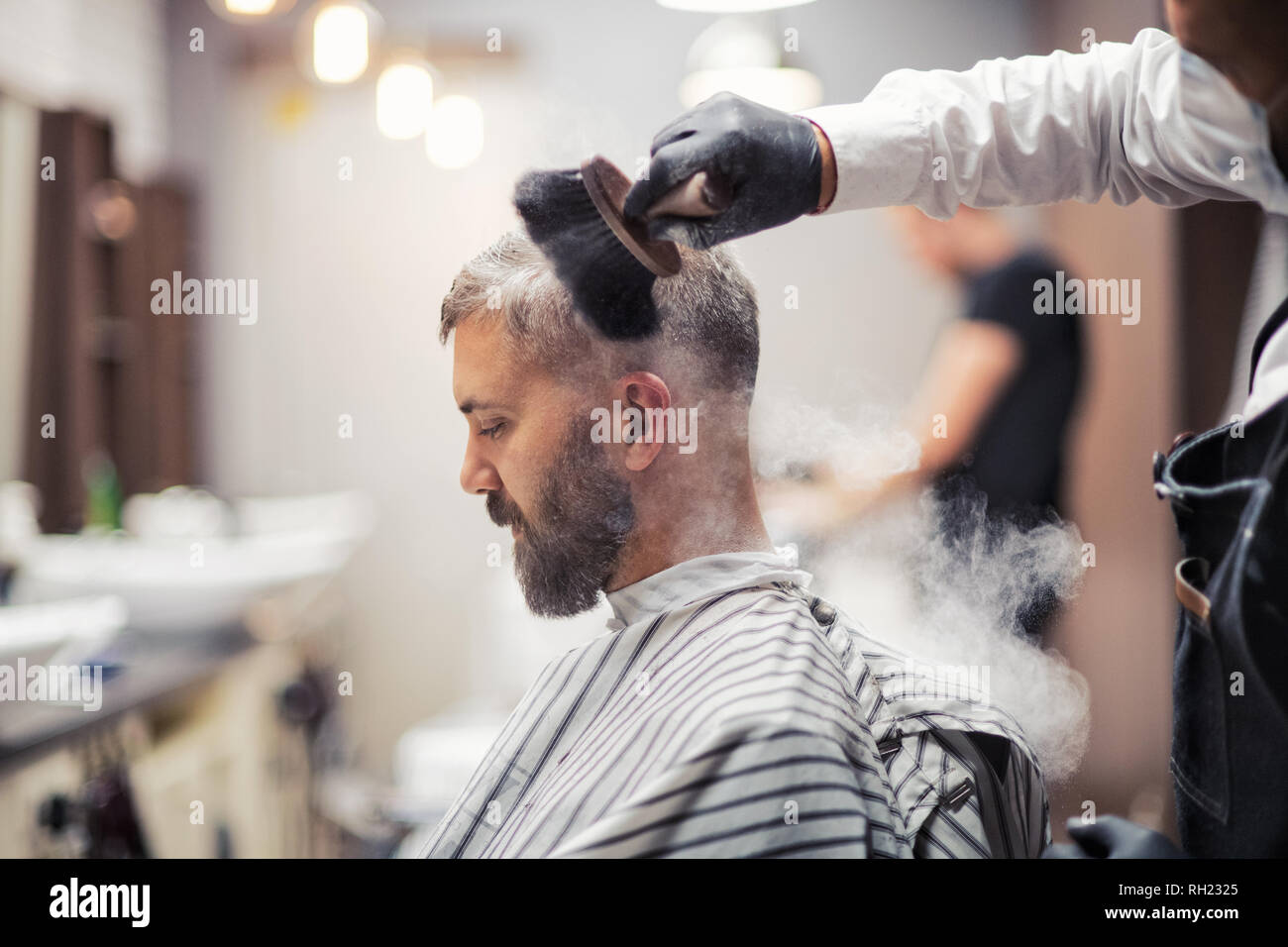 Handsome hipster man client visiting haidresser and hairstylist in barber shop, smoking a pipe. Stock Photo