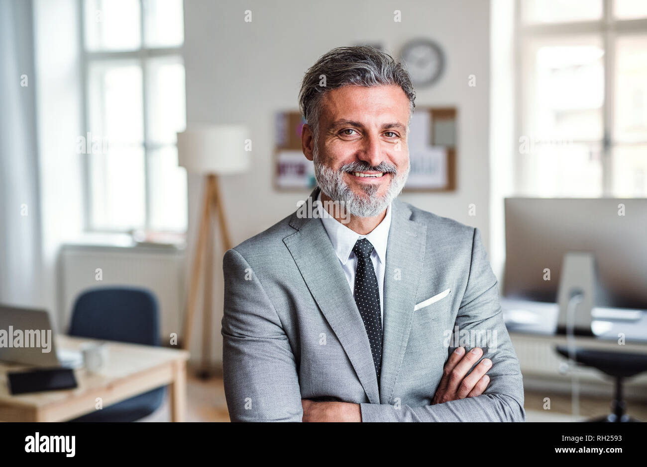 A cheerful mature businessman standing in an office, arms crossed Stock ...