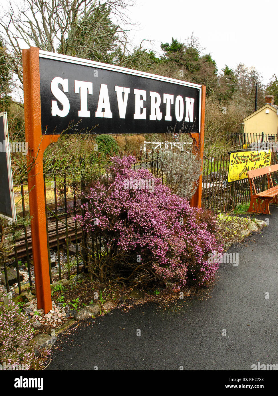 Staverton village railway station sign in Devon, with beautiful pink flowers growing under sign. Stock Photo