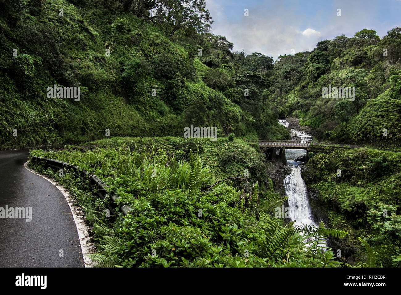 Road to Hana:  The Hana Highway turns to cross a one lane bridge beside a waterfall on the north coast of Maui. Stock Photo