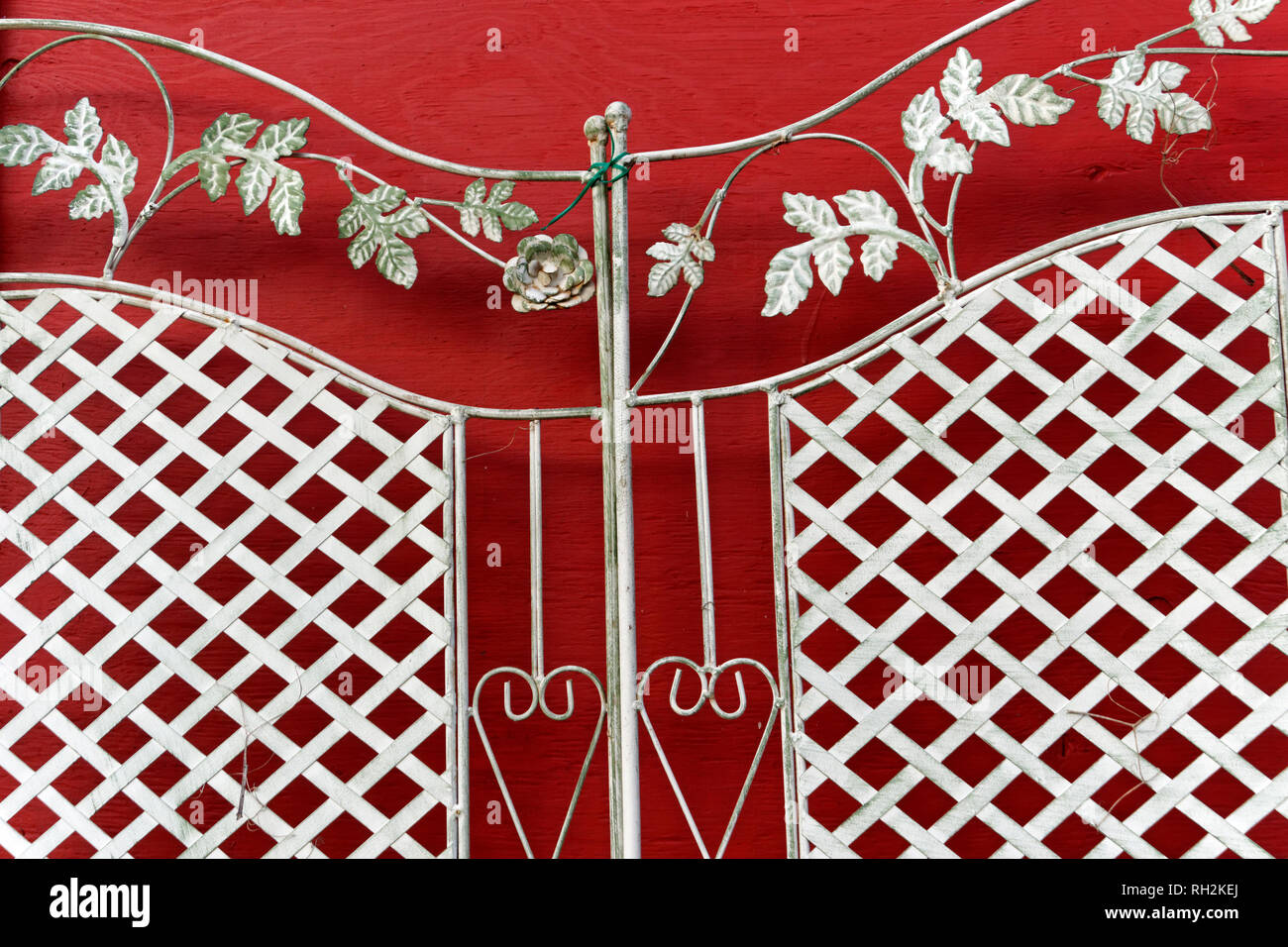 Ornate metal grill work with decorative floral design, hearts, and lattice against a  red wall Stock Photo