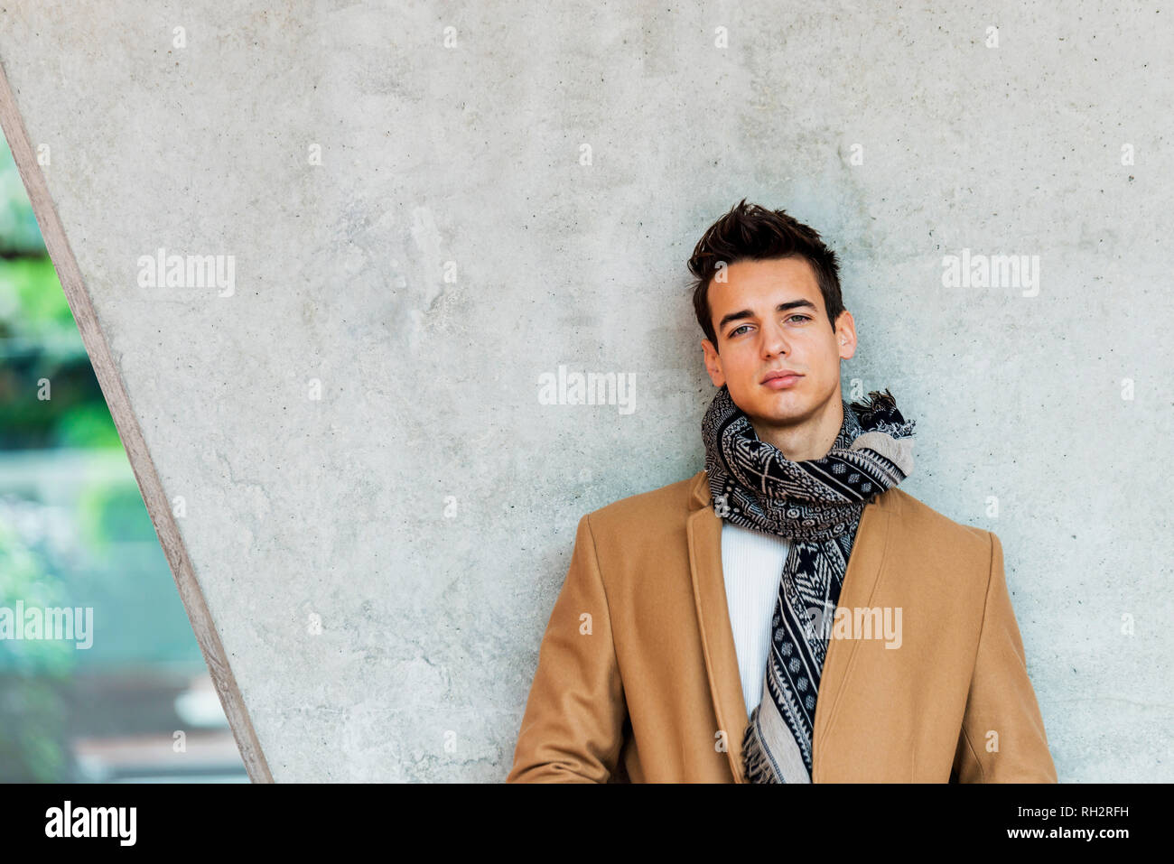 Front view of stylish young man wearing coat and scarf leaning on a ...