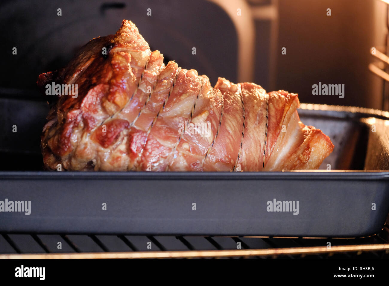 A roast delicious looking shoulder of pork cooking in an oven. The crackling is brown and crunchy  and the joint is held together with string Stock Photo