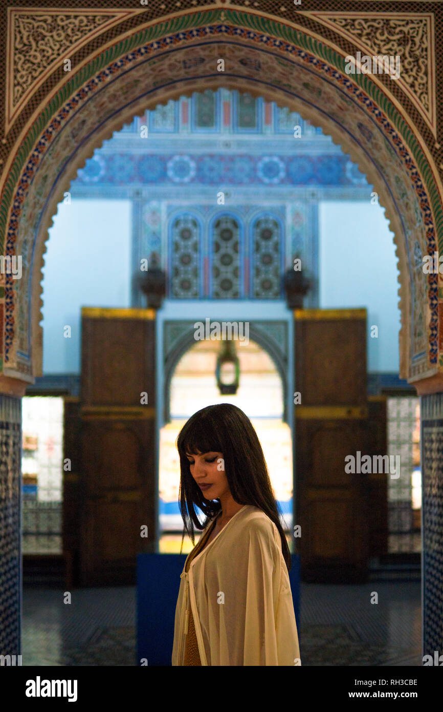 Beautiful Moroccan Girl in short golden dress and white mantle cloak in Rich interior of Picturesque Dar Si Said Riyad in Marrakech. Stock Photo