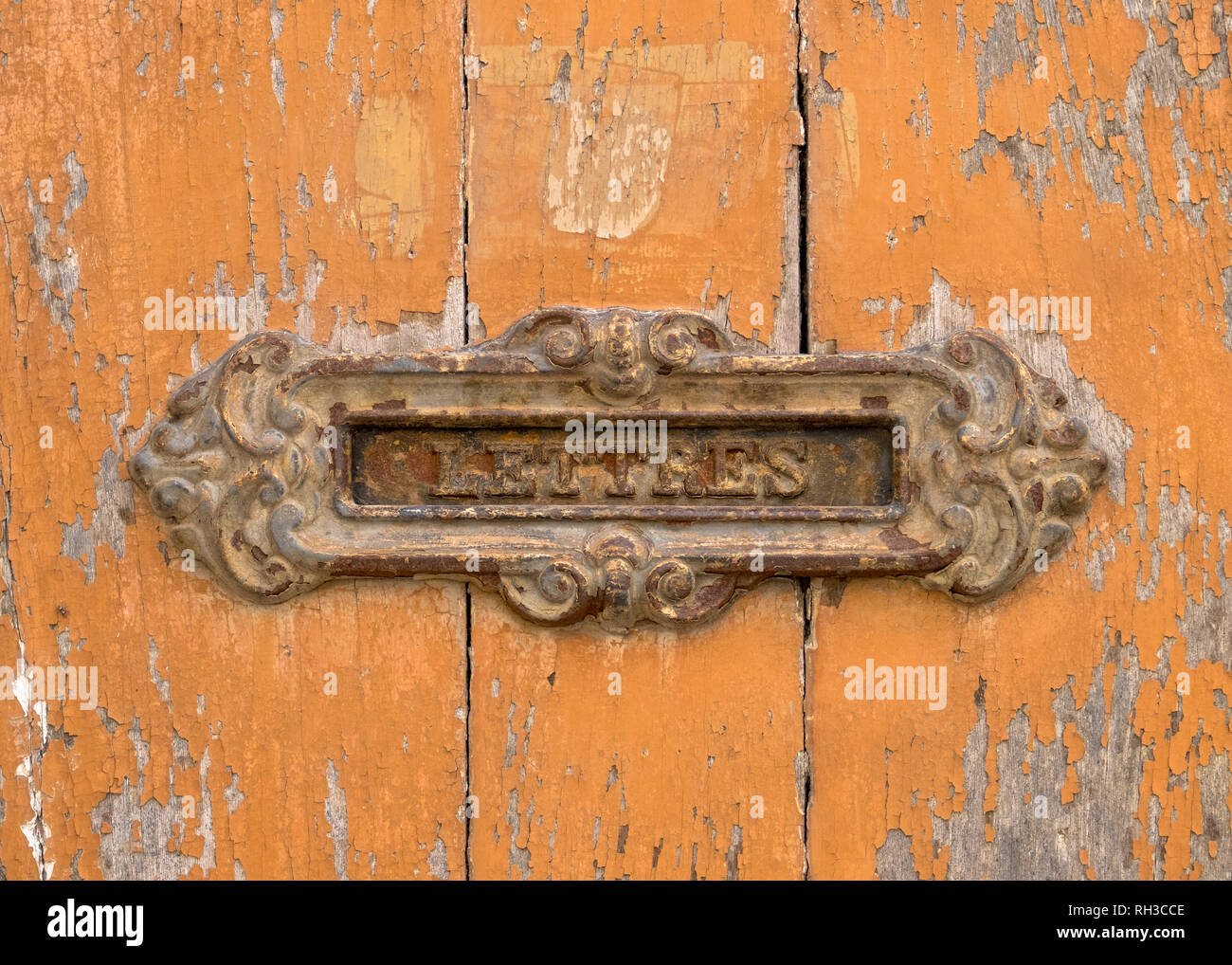 Rusted old French letter slot on orange peeling wood door.  Writing in French 'LETTRES' Stock Photo