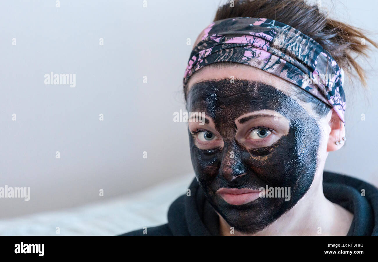 Woman doing beauty treatment having applied a black face mask looking at camera Stock Photo