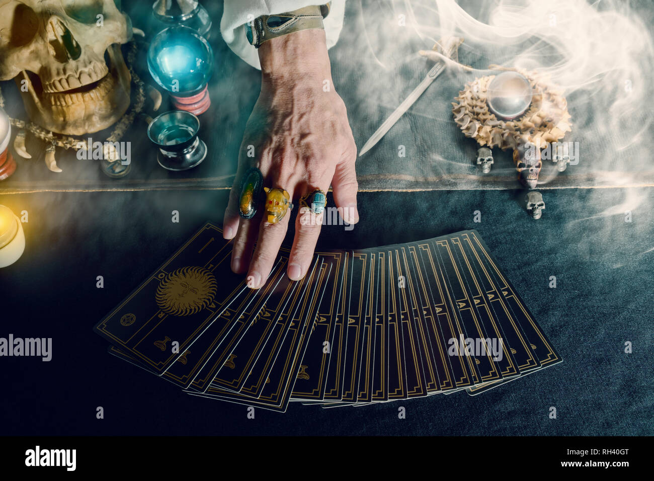 Hand of fortune teller and tarot card on the table under candlelight. Dark tone. Stock Photo