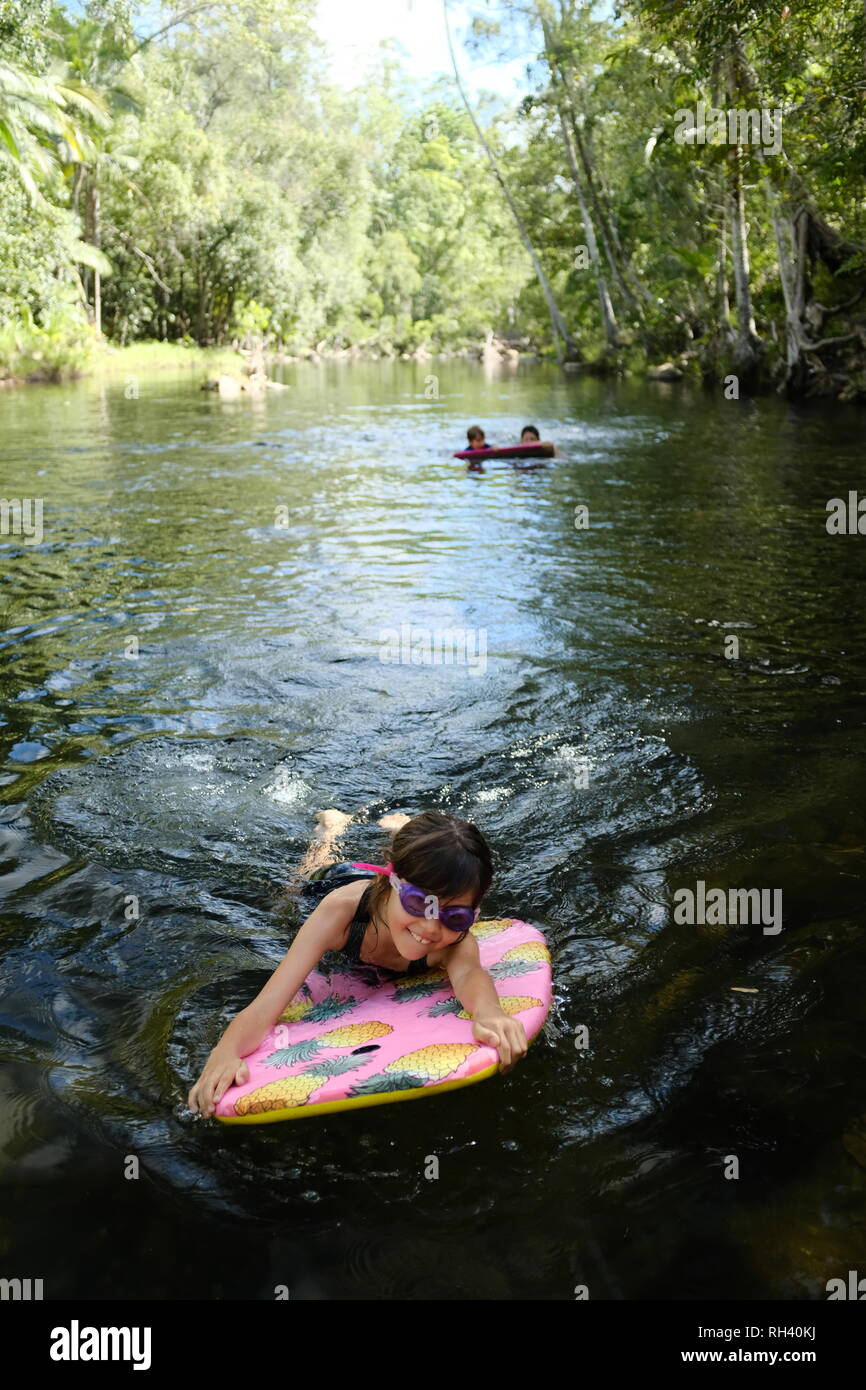 Young girl paddles on a boogie board with family in background, Finch Hatton, Queensland 4756, Australia Stock Photo