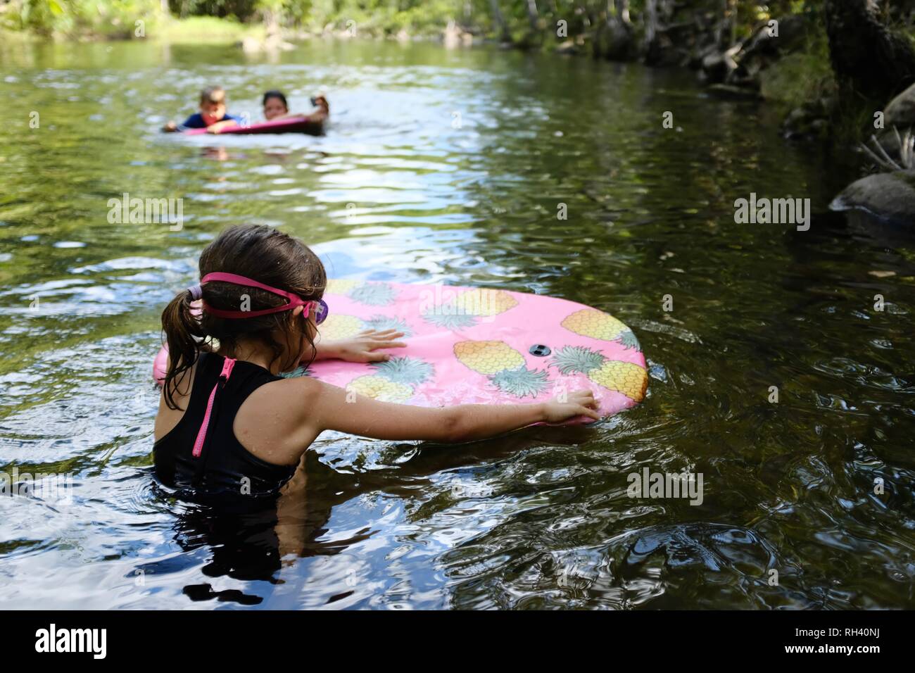 Young girl paddles on a boogie board with family in background, Finch Hatton, Queensland 4756, Australia Stock Photo