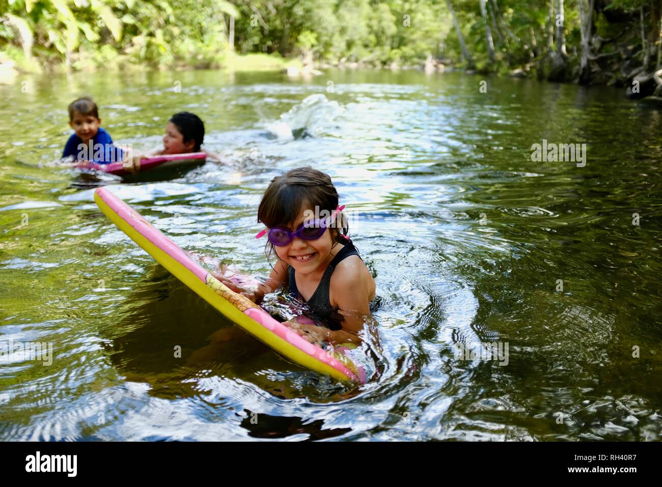 Young girl paddles on a boogie board with family in background, Finch Hatton, Queensland 4756, Australia Stock Photo