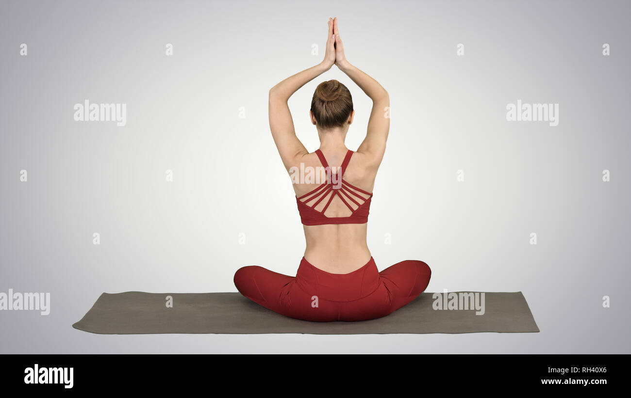 Young sporty woman sitting in lotus pose, join hands above her head on ...