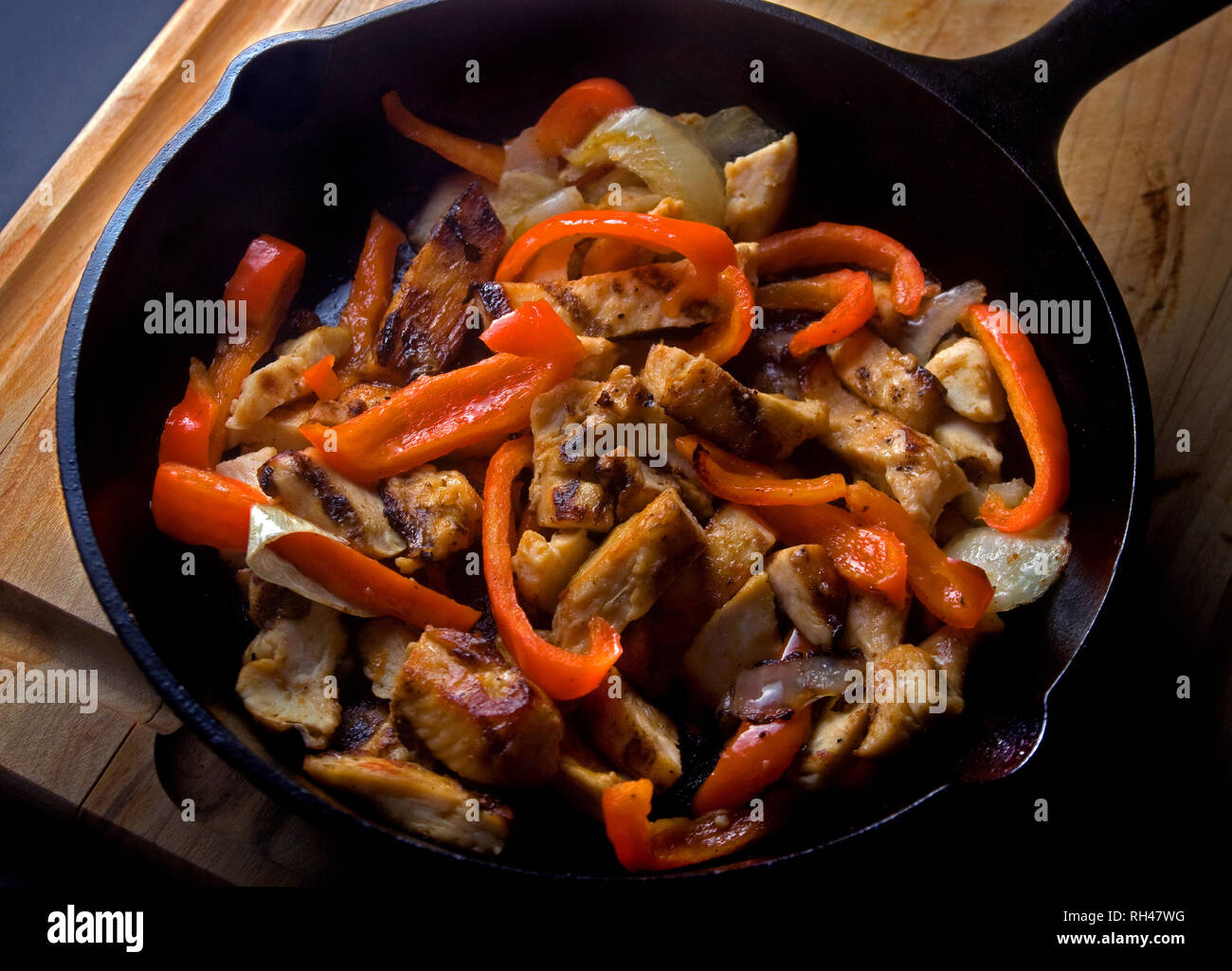 Boneless, skinless chicken is stir-fried with red and orange bell peppers and served in a cast iron skillet. Stock Photo