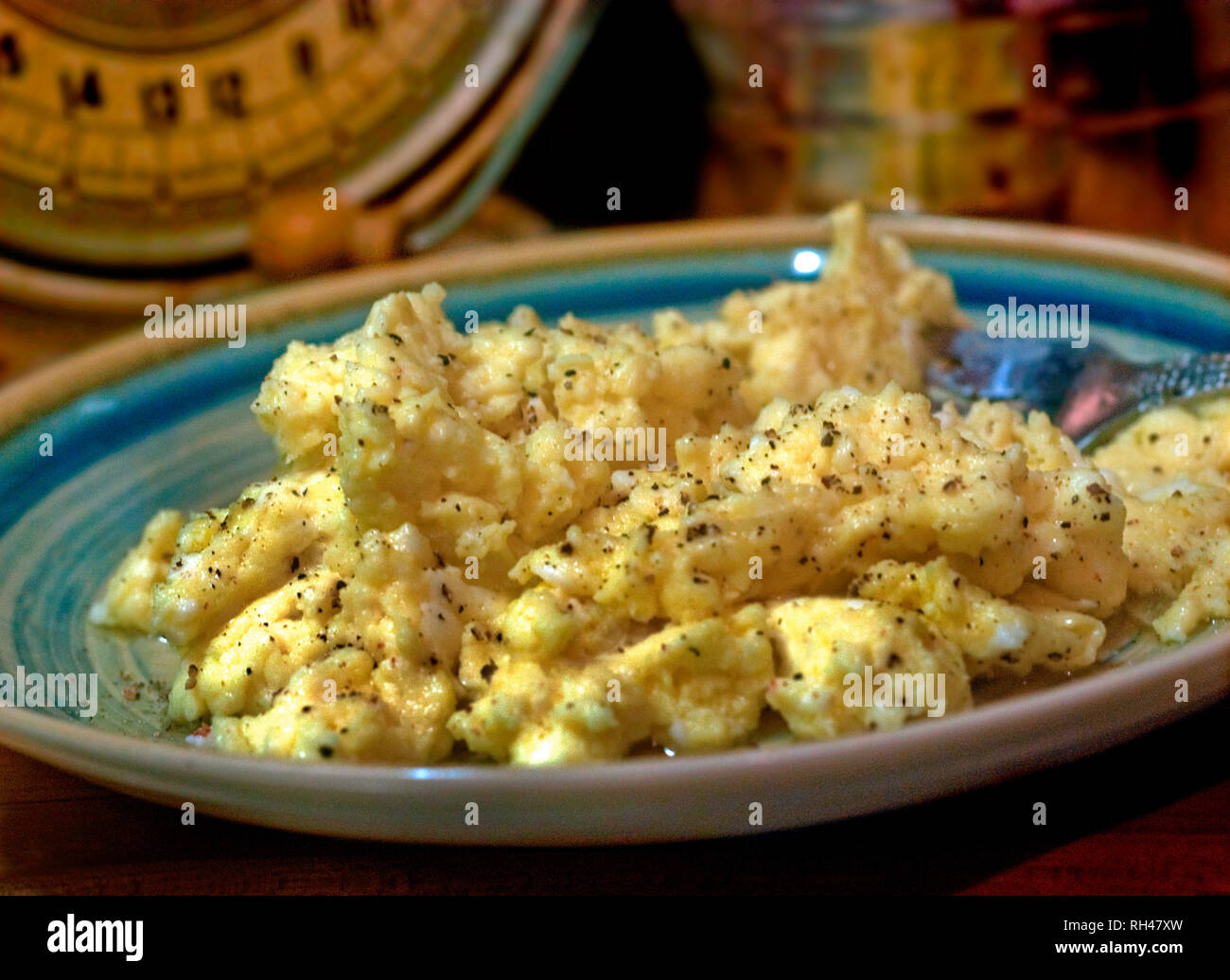Scrambled eggs, seasoned with salt and pepper, are pictured on a plate beside an antique scale. Stock Photo