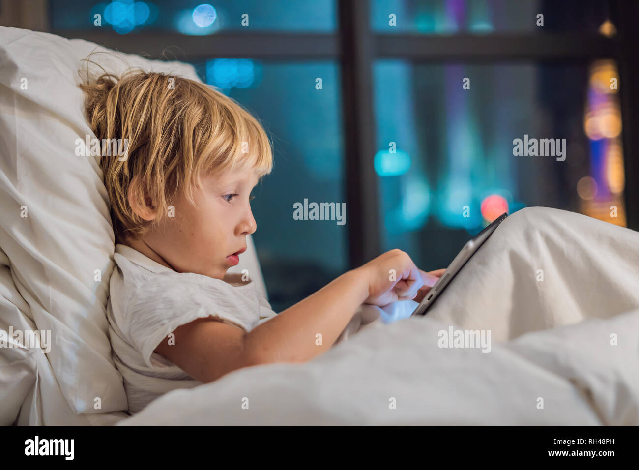 The boy uses the tablet in his bed before going to sleep on a