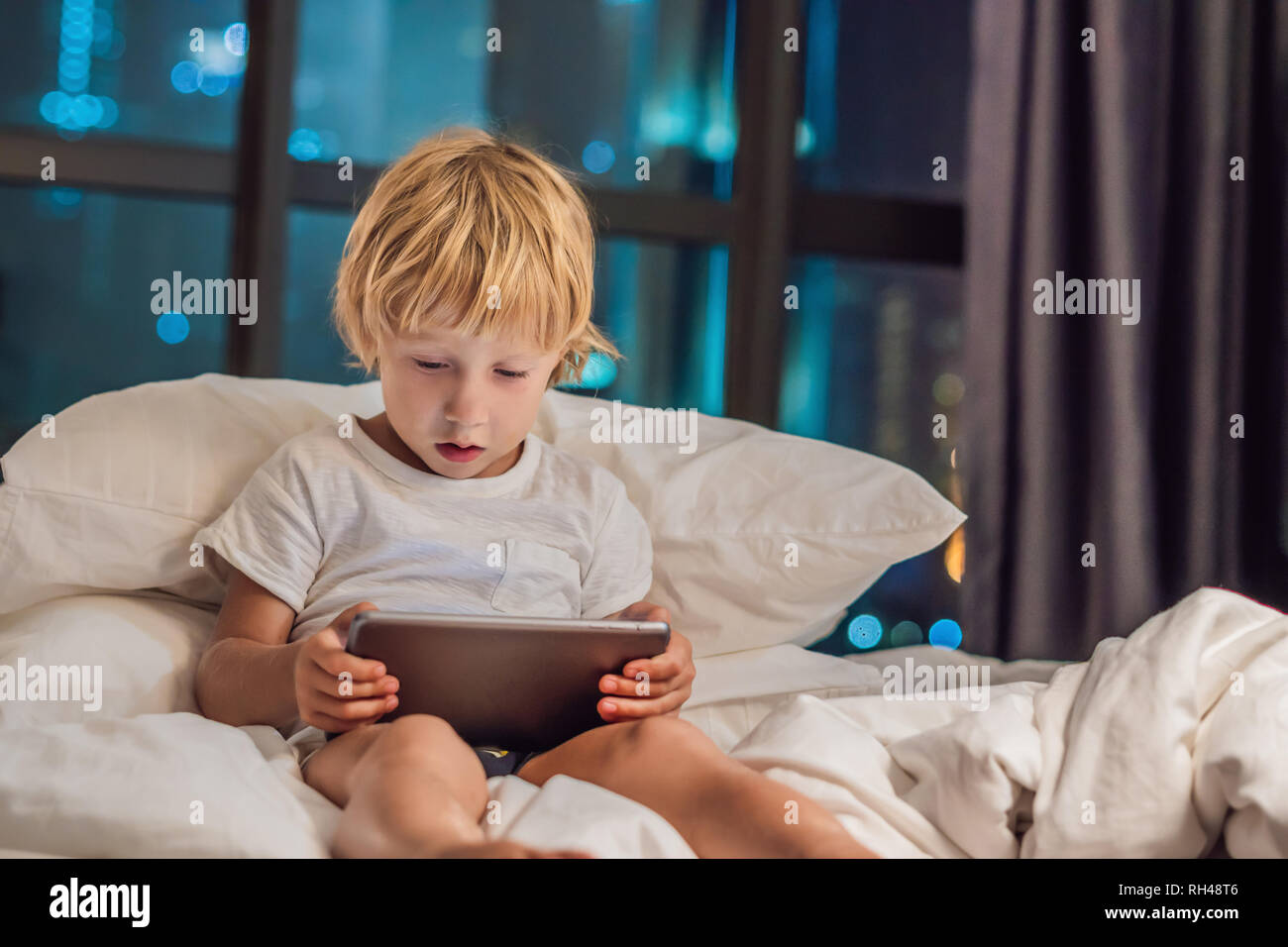 The boy uses the tablet in his bed before going to sleep on a