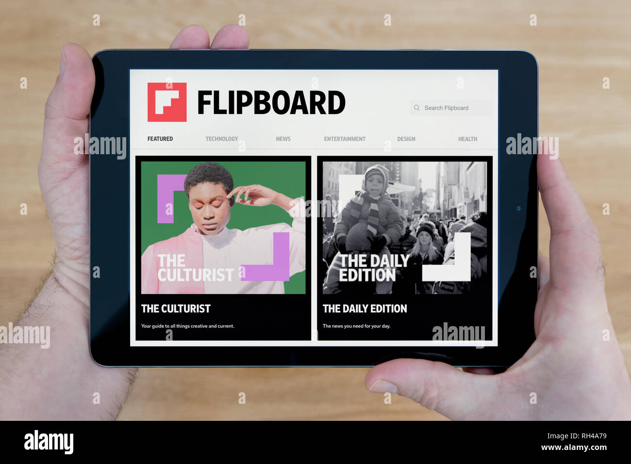 A man looks at the Flipboard website on his iPad tablet device, shot against a wooden table top background (Editorial use only) Stock Photo