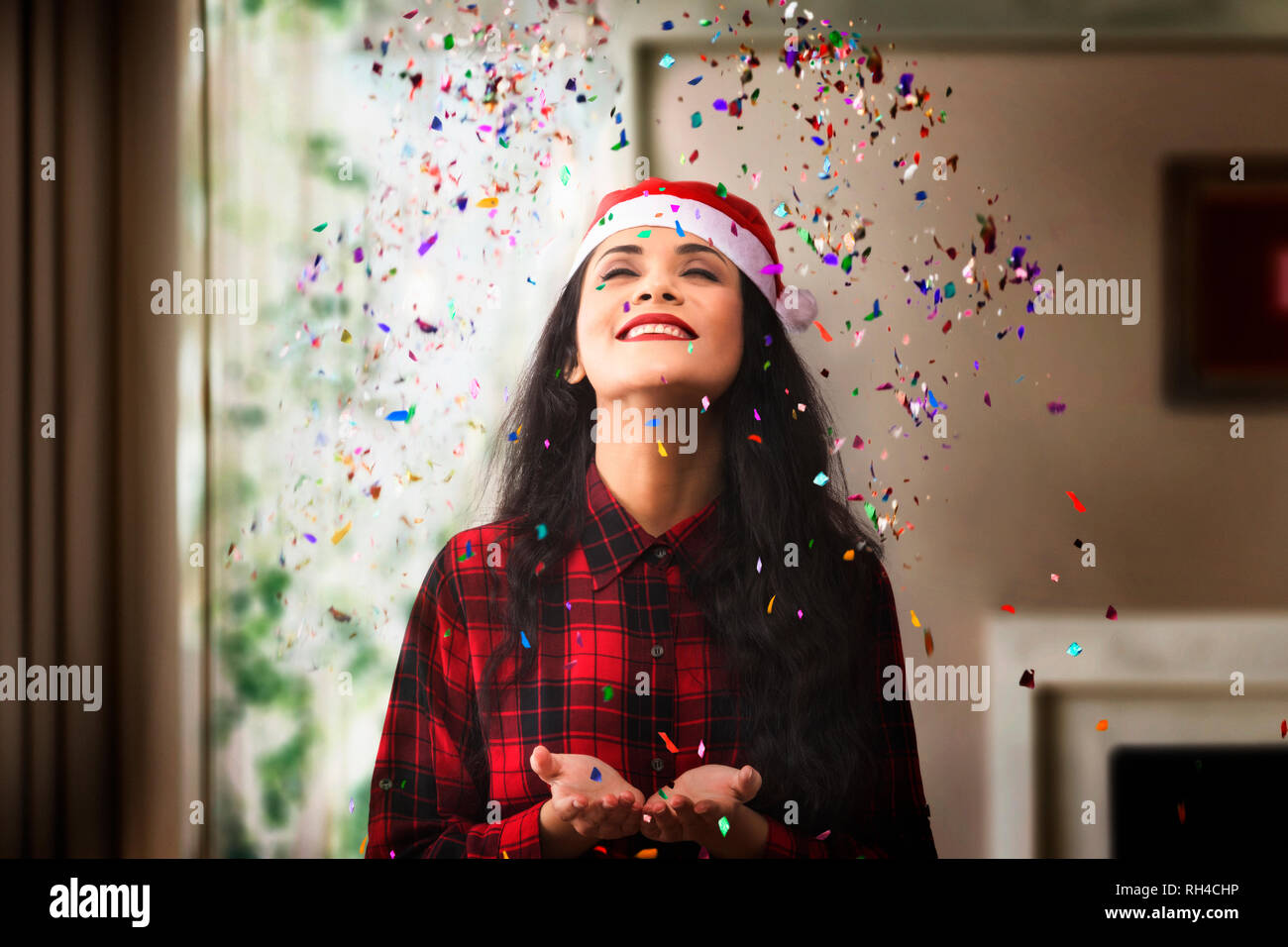 Close-Up Of Smiling Young Woman Throwing Confetti While Standing At Home During Christmas Stock Photo
