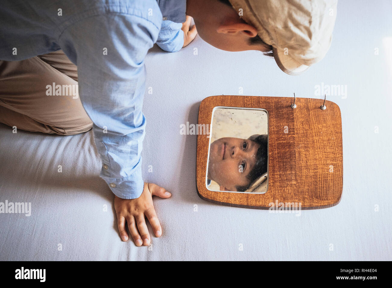 Boy looking at reflection in mirror on bed Stock Photo