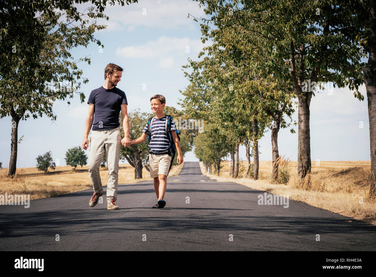 Father and schoolboy sun holding hands, walking down sunny road Stock Photo