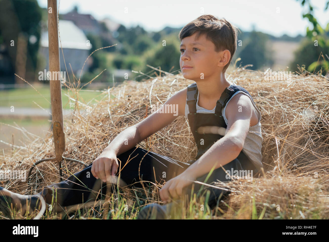 Boy in overalls sitting in hay on sunny farm Stock Photo