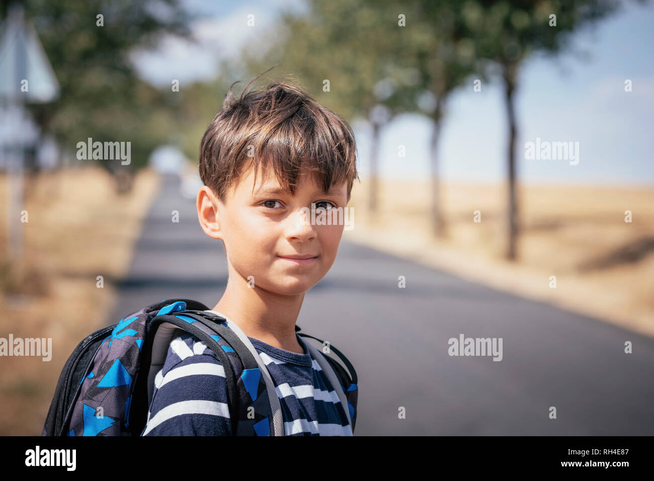 Portrait confident schoolboy with backpack on sunny road Stock Photo