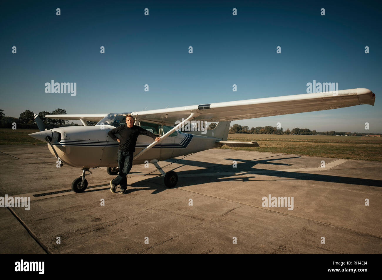 Portrait confident male pilot standing at small propellor airplane on sunny tarmac Stock Photo