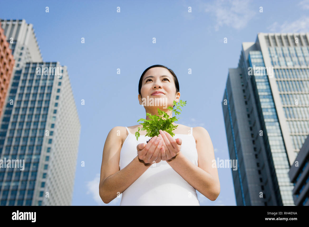 Portrait young woman holding green sapling below city highrises Stock Photo
