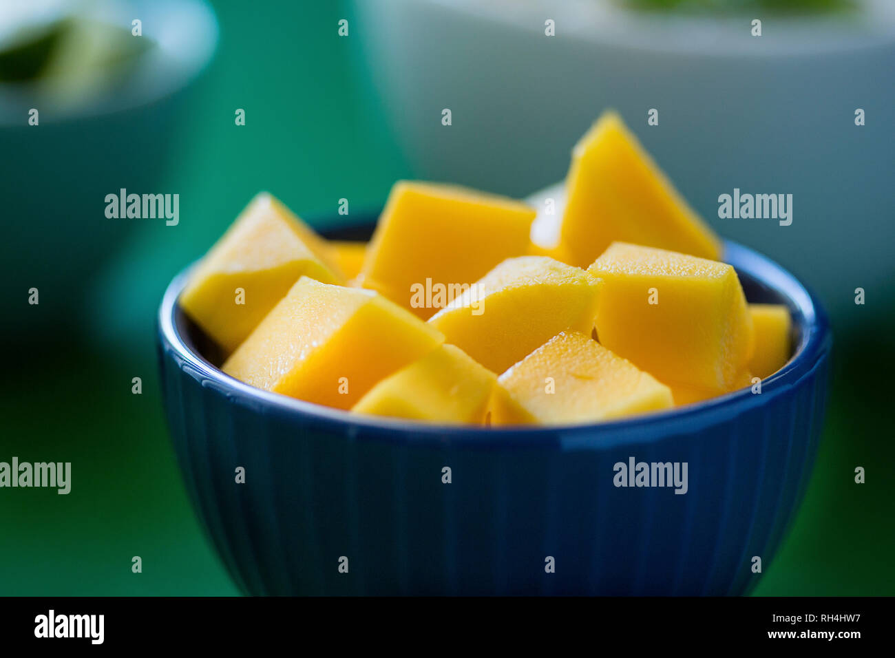 cut mango in blue bowl, other bowls of food in background Stock Photo