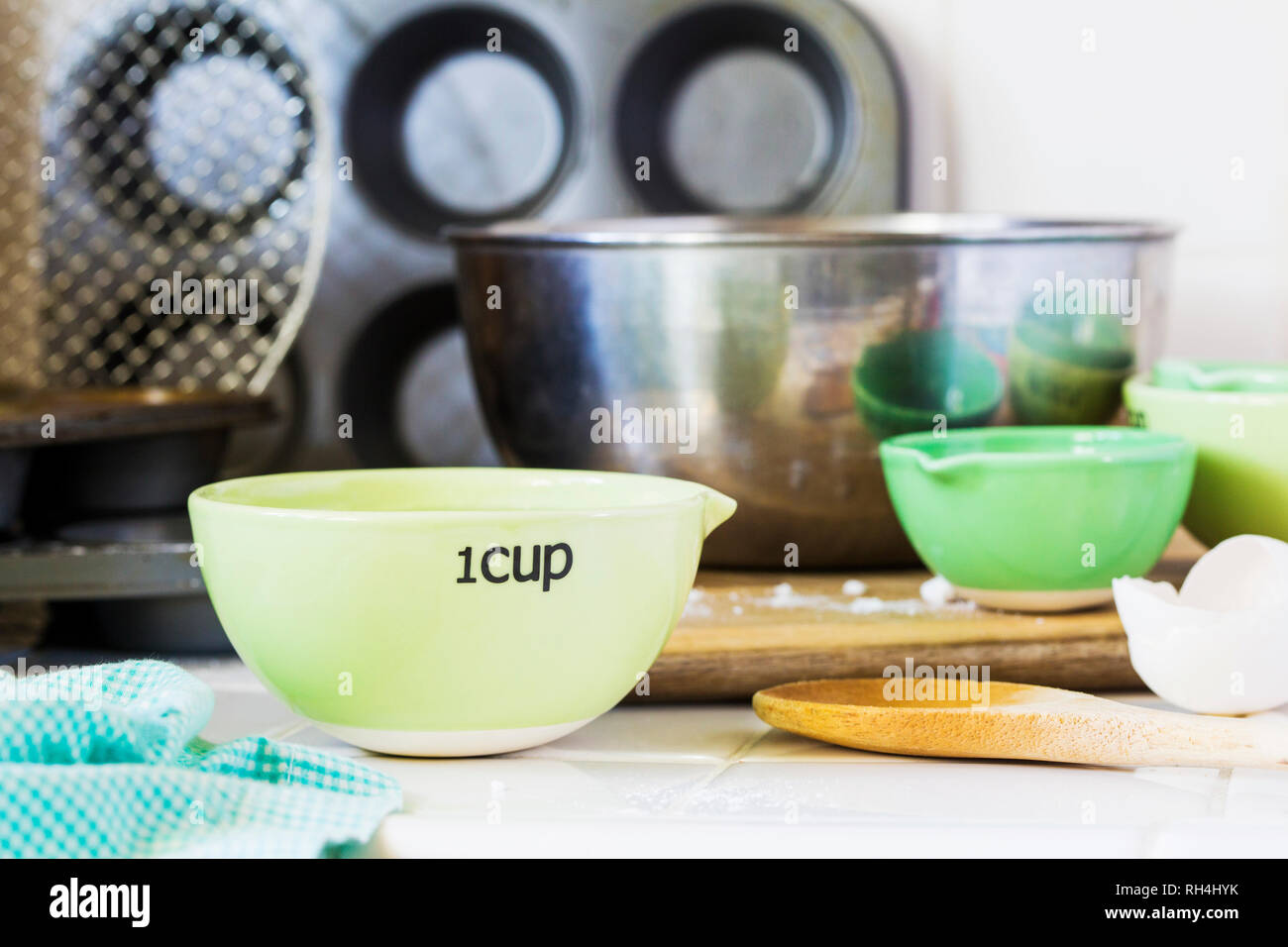 green measuring cups and metal mixing bowls on kitchen countertop with