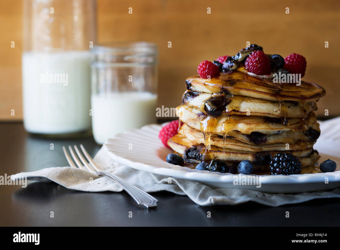 stack of pancakes on white antique plate with syrup and mixed berries and milk in mason jar. Stock Photo