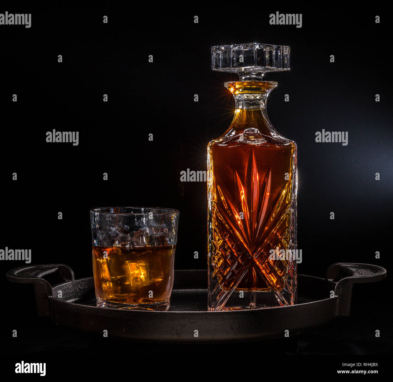 liquor decanter and glass on cast iron serving tray with ice cubes
