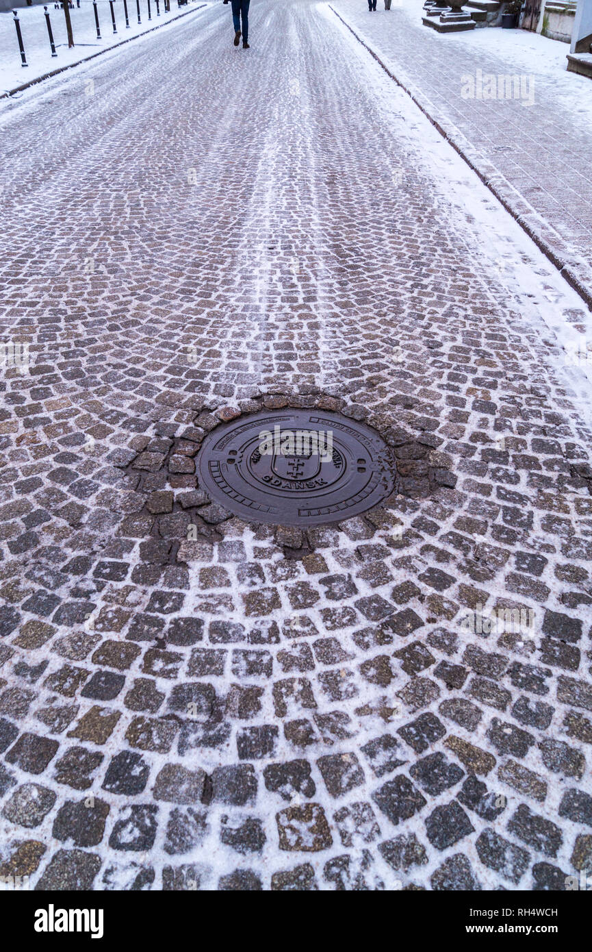 Municipal drain cover anv view of cobbled street and the Great Armoury, 1609, now Academy of Fine Arts, Ulica Piwna, Gdańsk, Poland Stock Photo