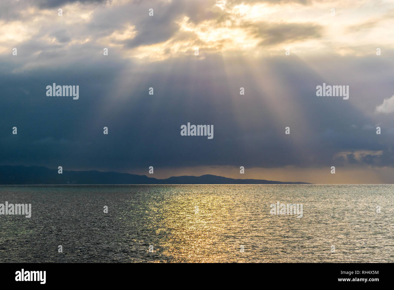 Scenic landscape ocean mountain silhouette view of sun rays bursting through clouds. Concept of breakthrough, hope, signs. Stock Photo