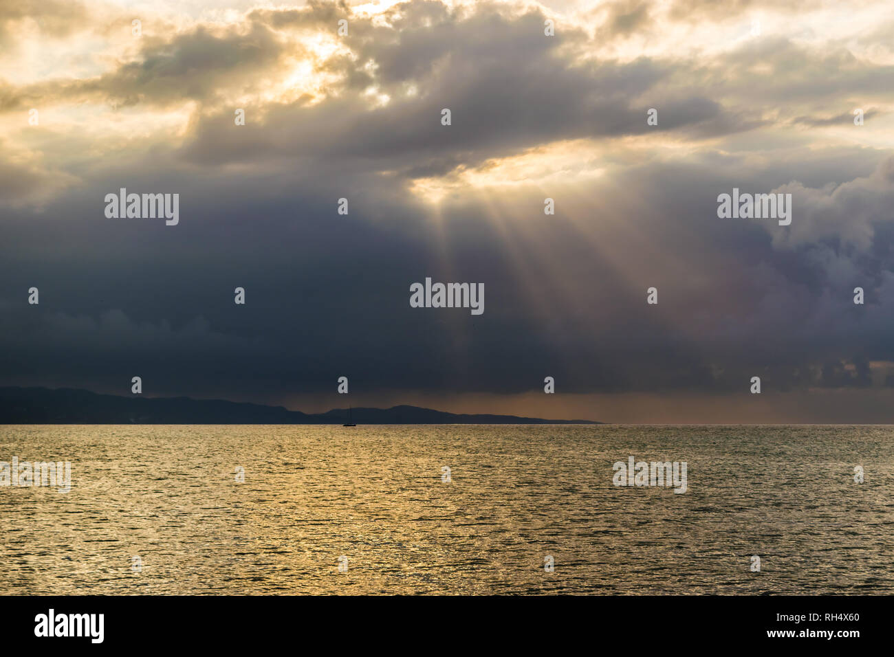 Scenic landscape ocean mountain silhouette view of sun rays bursting through clouds. Concept of breakthrough, hope, signs. Stock Photo