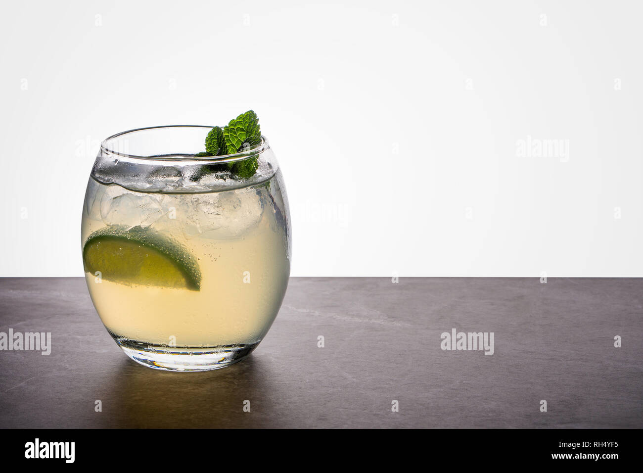 A mojito cocktail in a small oval glass garnished with mint and lime on a  stone rock base and back lit background Stock Photo - Alamy